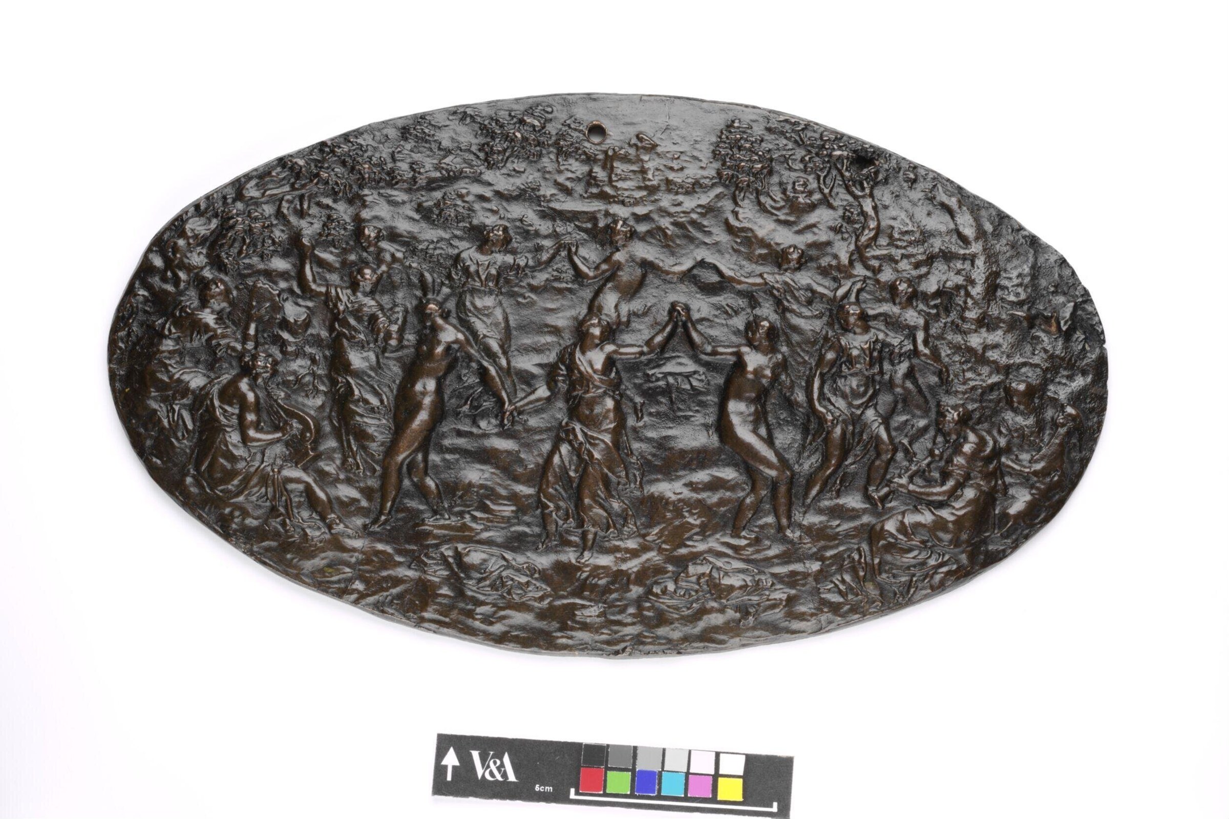 Bronze oval plaquette crowded with nude and semi-draped female figures in varied poses of movement and celebration across a rocky landscape.