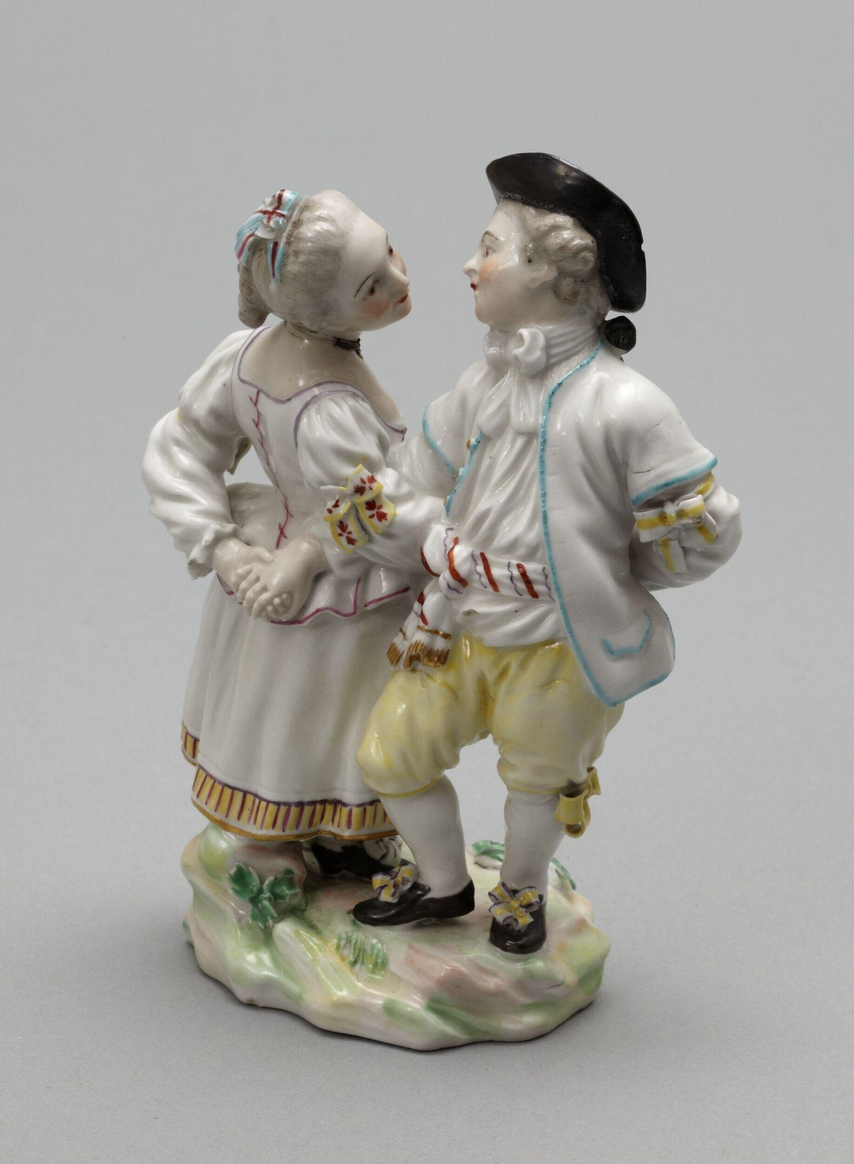 Two young dancers in white linen and yellow breeches face each other in formal upright posture on a rocky ground, rendered in glazed porcelain.