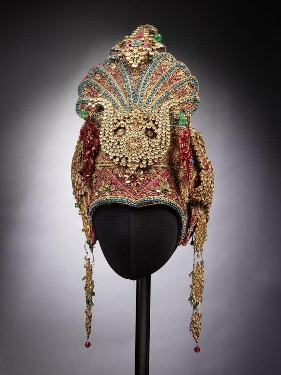 Ornate Russian kokoshniki headdress on display bust, gold metalwork studded with pearls and rubies, with burgundy silk panel and trailing gem-drop ornaments.