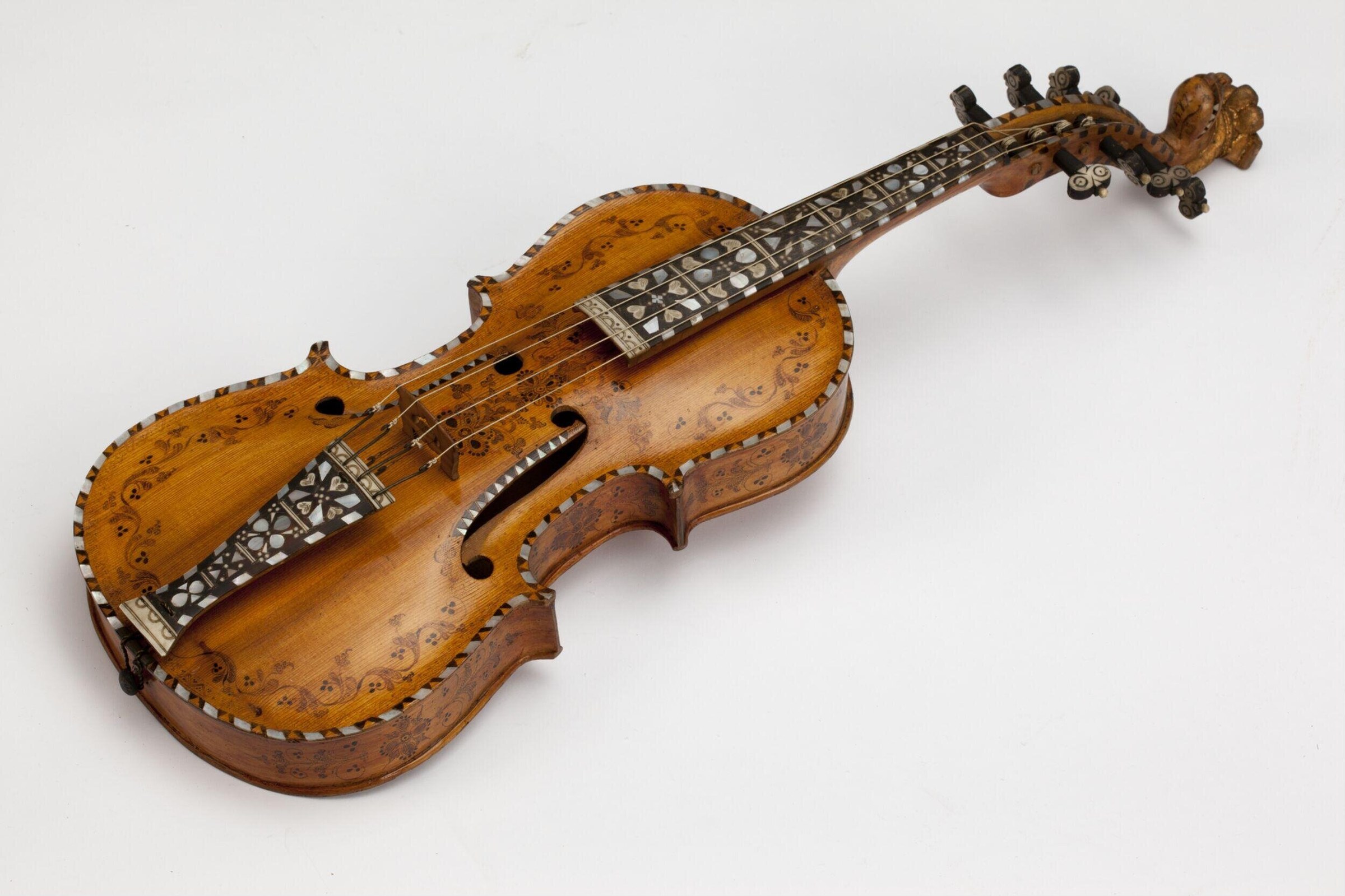 A carved wooden Hardanger fiddle with decorative bone inlay, photographed against a neutral background.