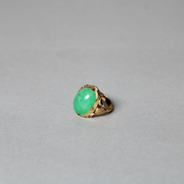 Gold ring with large oval green stone cabochon on neutral grey ground.