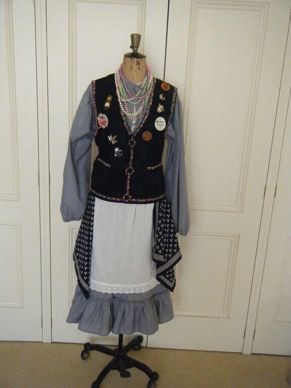 Complete North West Morris costume on dress form: black embroidered waistcoat with badges, blue shirt, white apron, grey ruffled skirt, patterned shawl, pearl