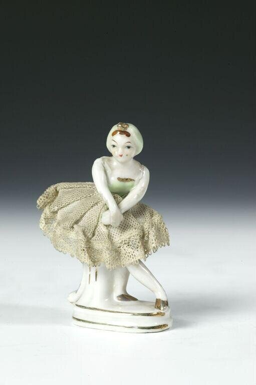 Porcelain figurine of a female ballerina in white bodice and cream lace skirt, standing in a classical pose on a simple base.