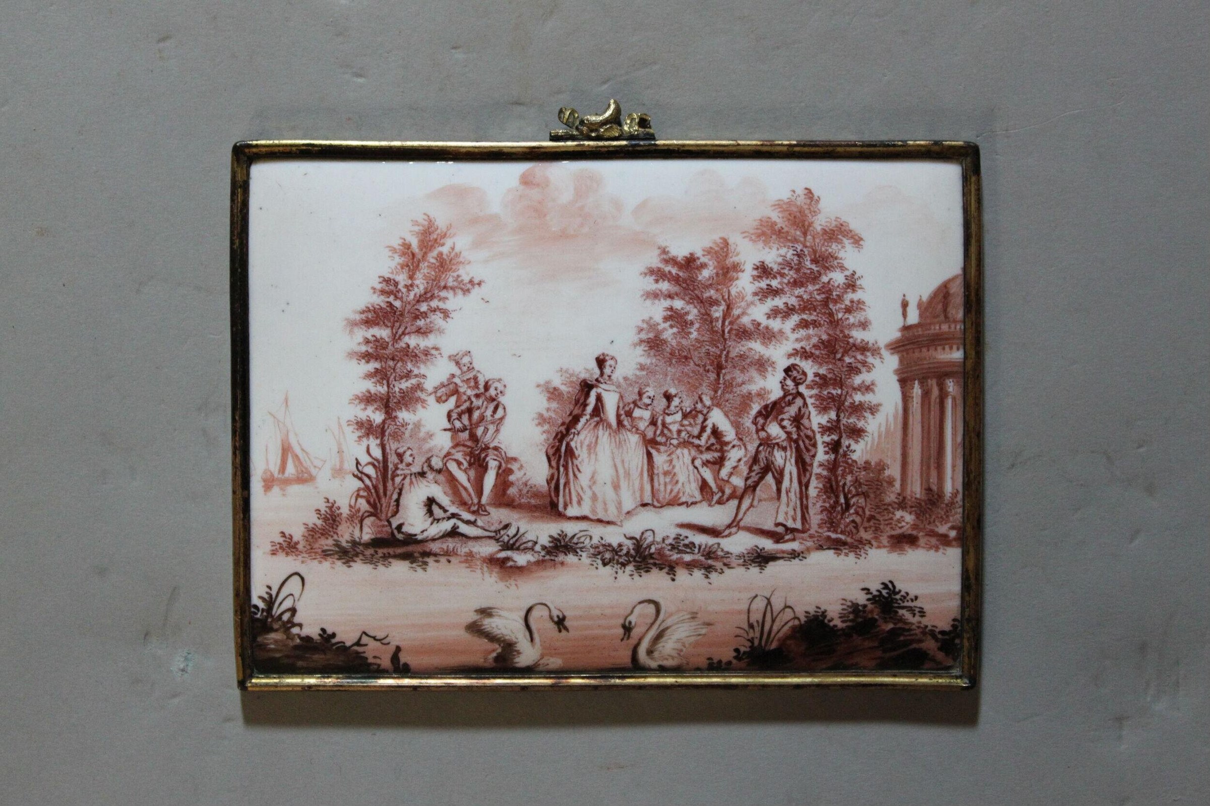 Sepia porcelain plaque in brass frame: aristocratic garden with woman in white gown centered; attendants and reclining admirer around her; swans, trees