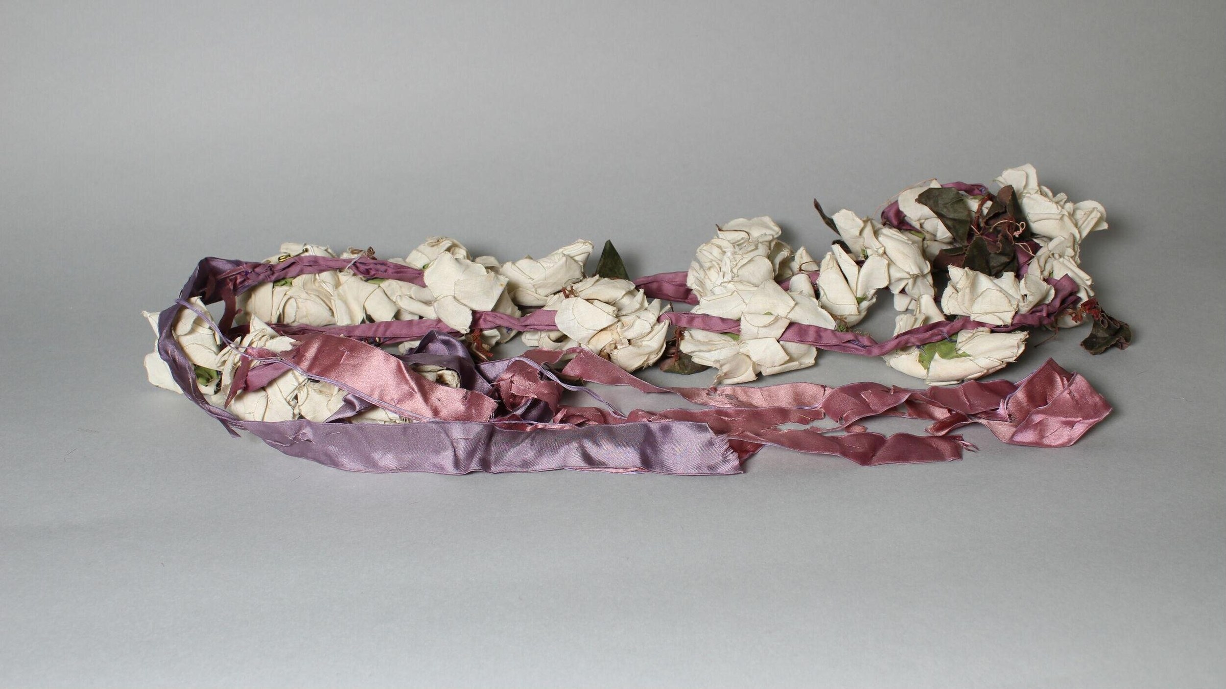 Photograph of cream silk petals and mauve ribbons arranged as dismantled costume components on a neutral ground.