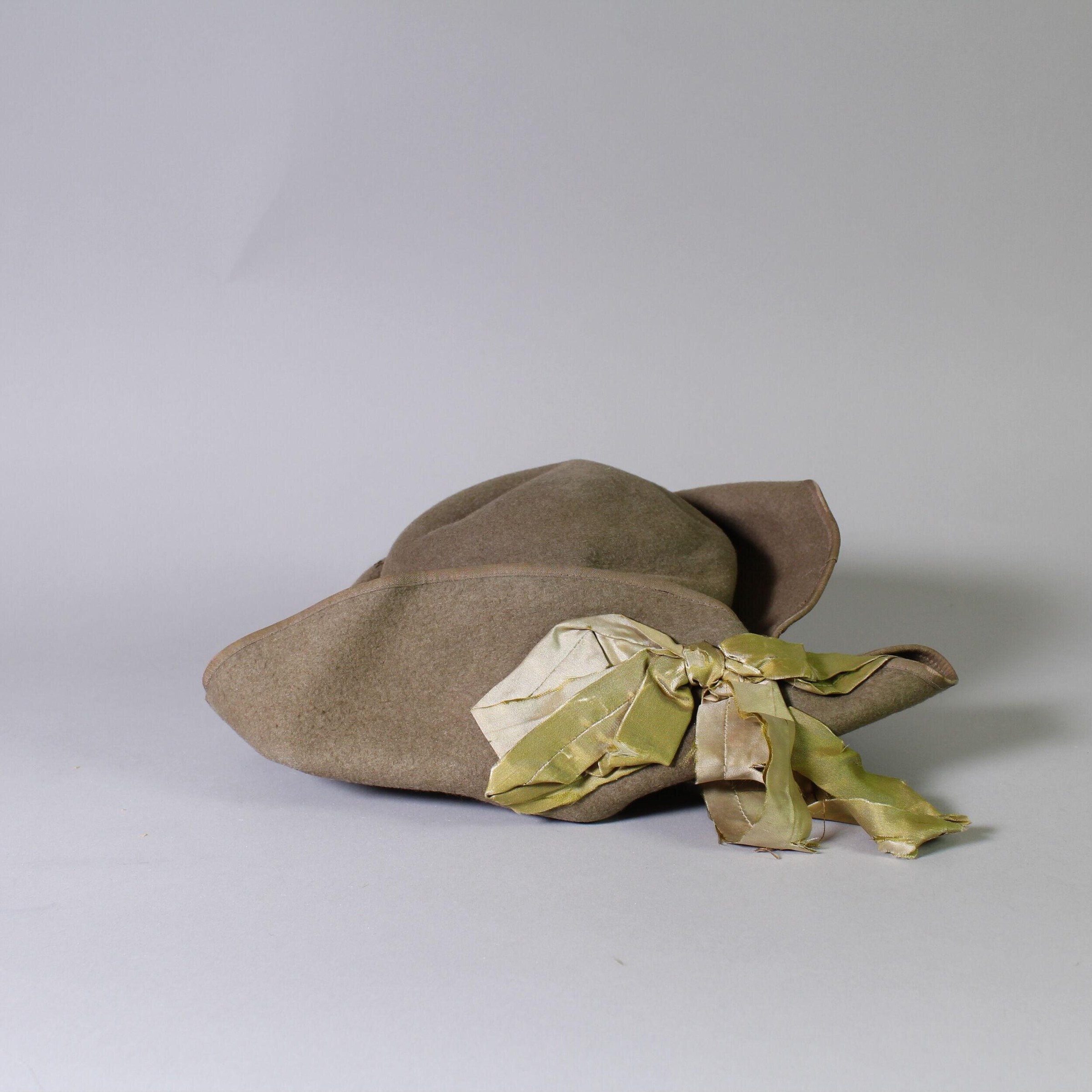 Draped tan wool stage costume with green silk accent, arranged on neutral surface and photographed for archive documentation.