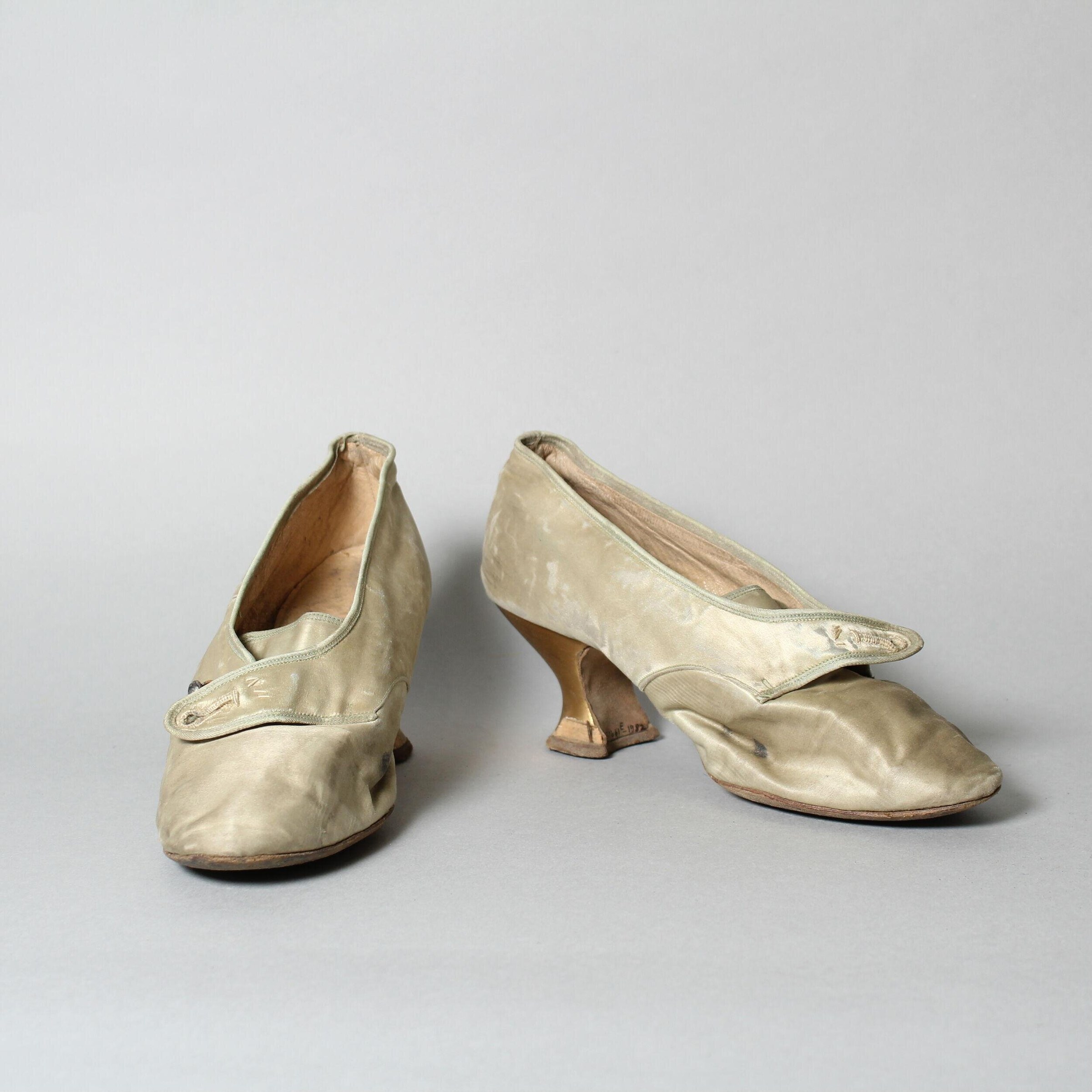 Pair of cream silk heeled court shoes with slender heels, shown from rear and profile views, circa 1912.