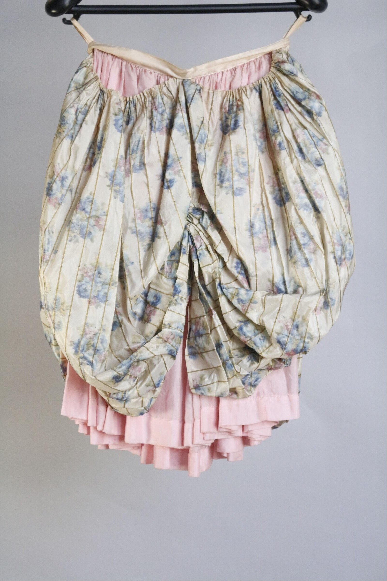 Layered theatre skirt with cream floral-printed outer layer and pink linen underskirt, gathered at waist, on a dress form.