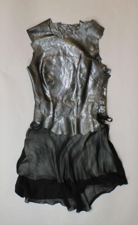 Crumpled silver and black theatrical costume photographed flat, creases recording movement of unseen dancer.
