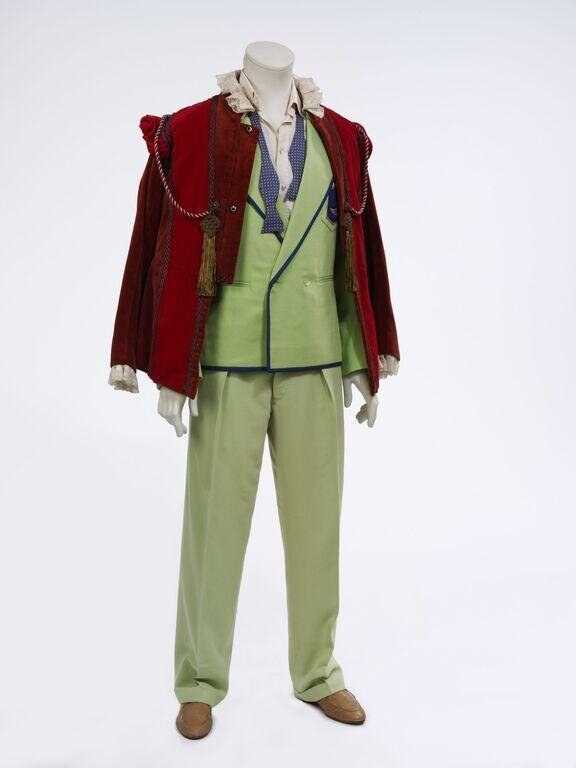 Lime-green double-breasted suit with navy-patterned shirt, worn under dramatic wine-red velvet coat with gold rope fastenings, displayed on mannequin.