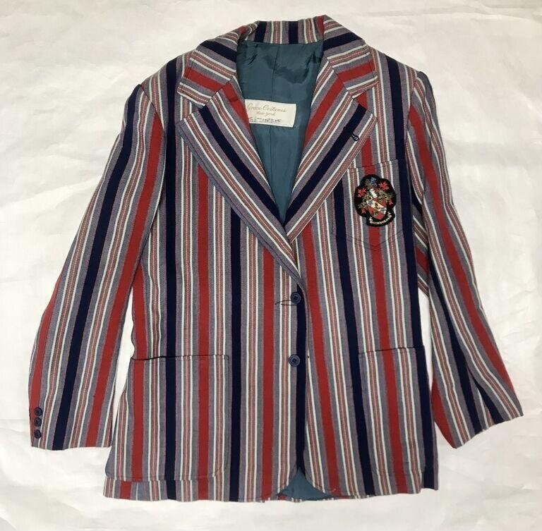 Striped double-breasted tailored jacket in navy, burgundy, and cream, displayed flat with teal lining visible and a jewelled badge on the left chest.