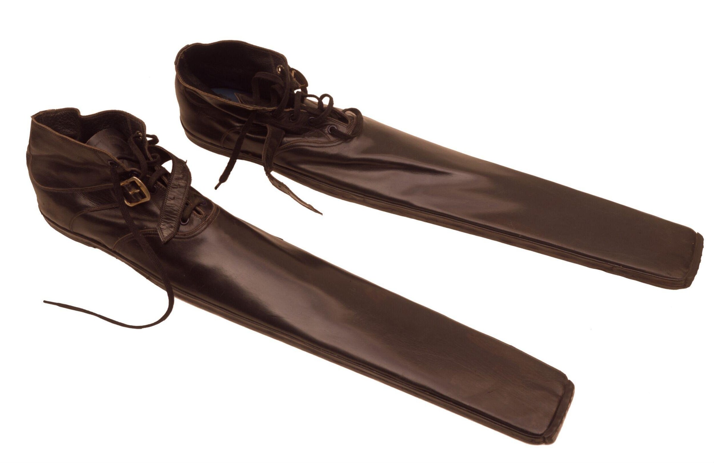 Two brown leather theater boots with buckled ankle straps, each with an elongated leg covering, displayed against a white background.