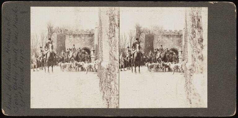 Stereoscopic photograph of mounted huntsmen and a pack of hounds assembled before a medieval abbey gatehouse, 1912.
