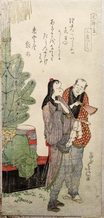 Two Japanese performers in loose robes gesture toward each other beside a decorated drum and pine sapling, from an Edo-period woodblock print.