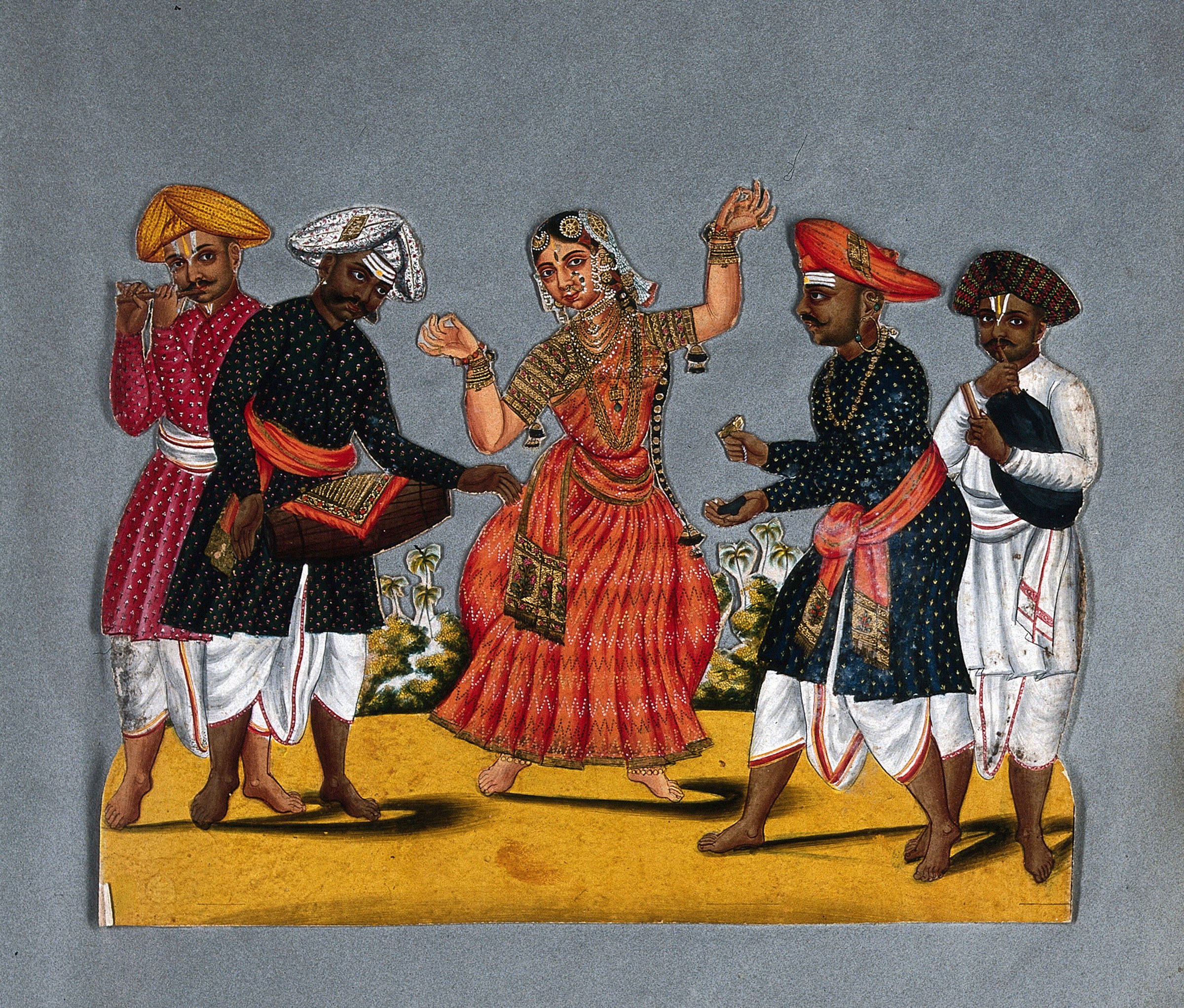 A South Indian dancer in a red-orange embroidered sari performs with raised arm, surrounded by four male musicians in court dress holding instruments.