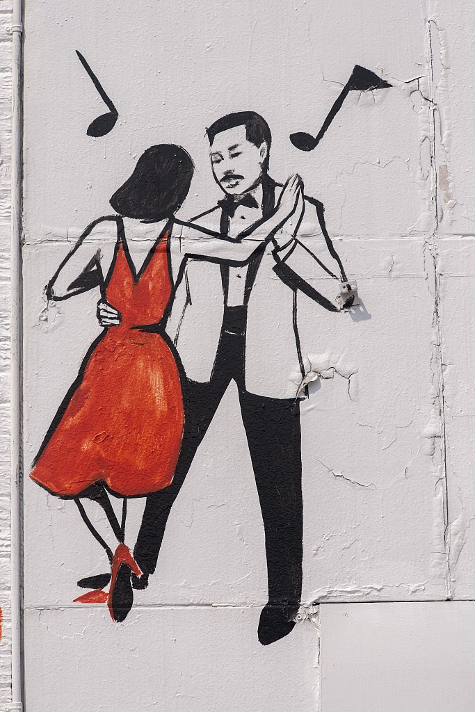 Mural of couple in formal wear mid-ballroom dance; woman in red dress airborne, man in tuxedo supporting. Musical notes float above.