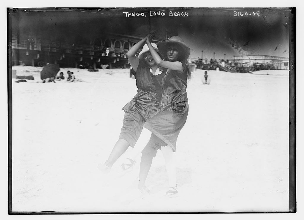 Two dancers in a close embrace perform tango on a sandy beach, the woman leaning dramatically backward with her leg extended.