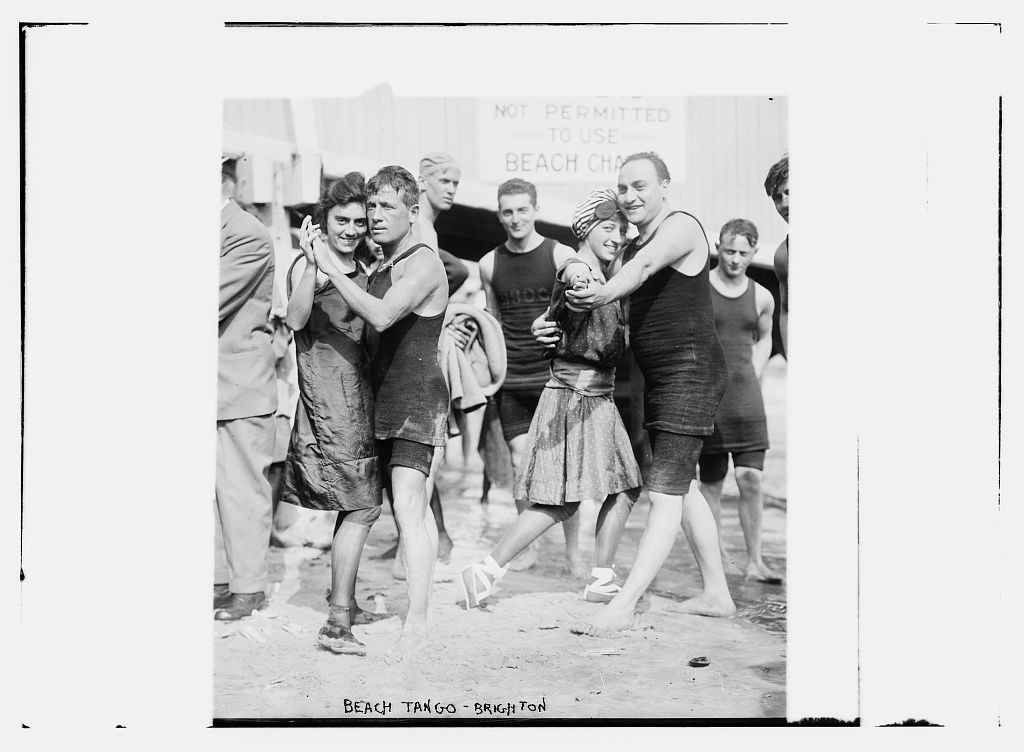 A group of bathers in swimming costumes dance in close pairs on wet sand at Brighton beach, circa 1910.