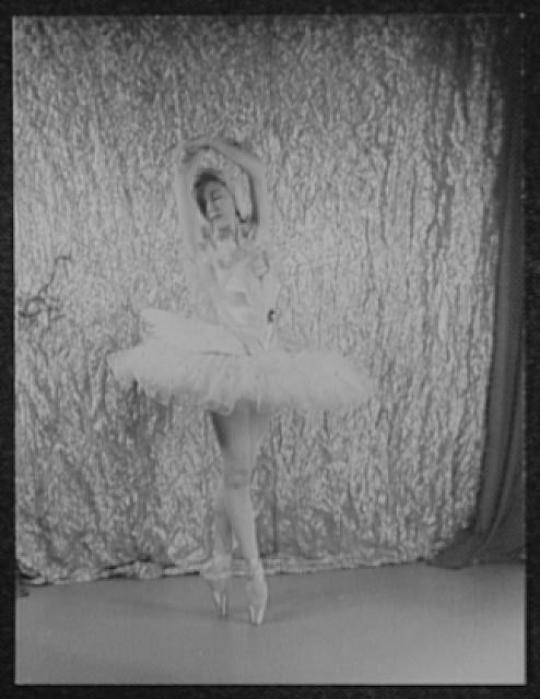 Alicia Markova in white tutu and pointe shoes stands in classical ballet pose against a draped backdrop, 1948.
