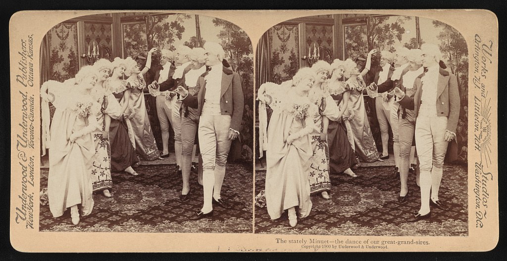 Two couples in 18th-century costume stand in a formal ballroom, posed for a stereoscopic dance photograph dated 1900.