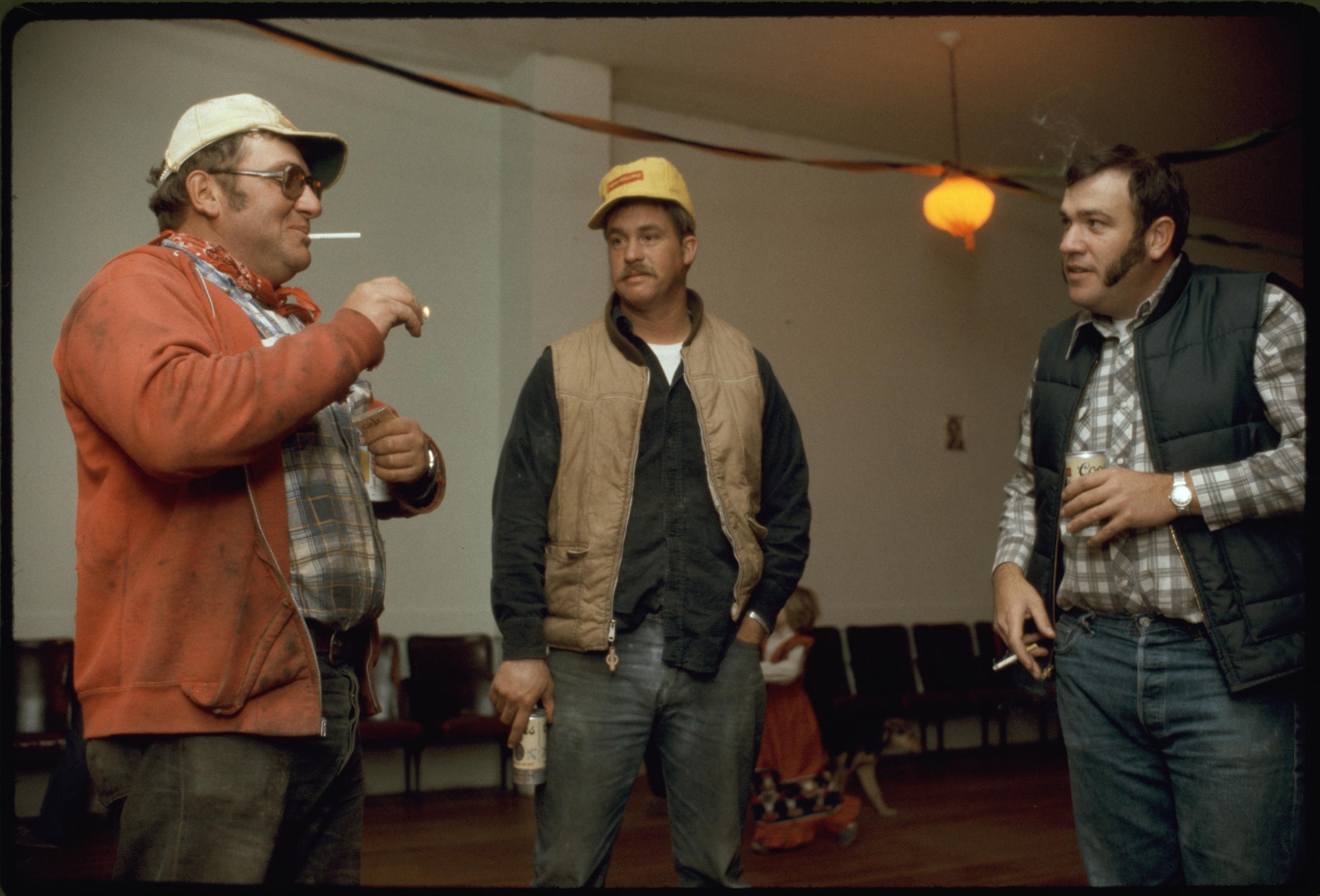 Three men in work clothes stand in an empty community hall, preparing the space for a dance.