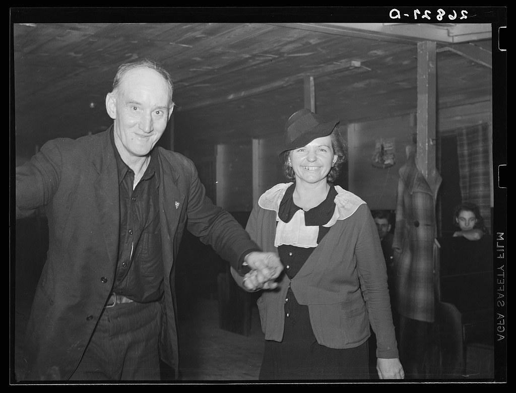 Two middle-aged dancers in casual dress smile at the camera during a pause in their dance at a rural Illinois dance hall, 1939.