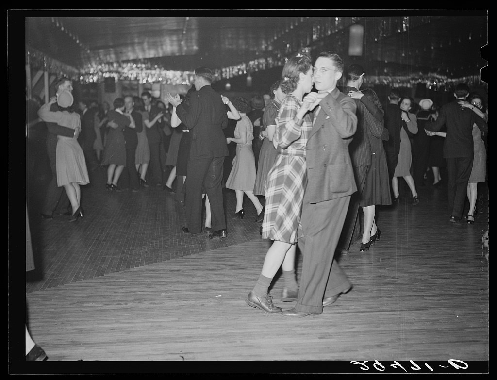 Black-and-white photograph of a crowded dance hall with couples dancing in close embrace beneath string lights, circa 1940.