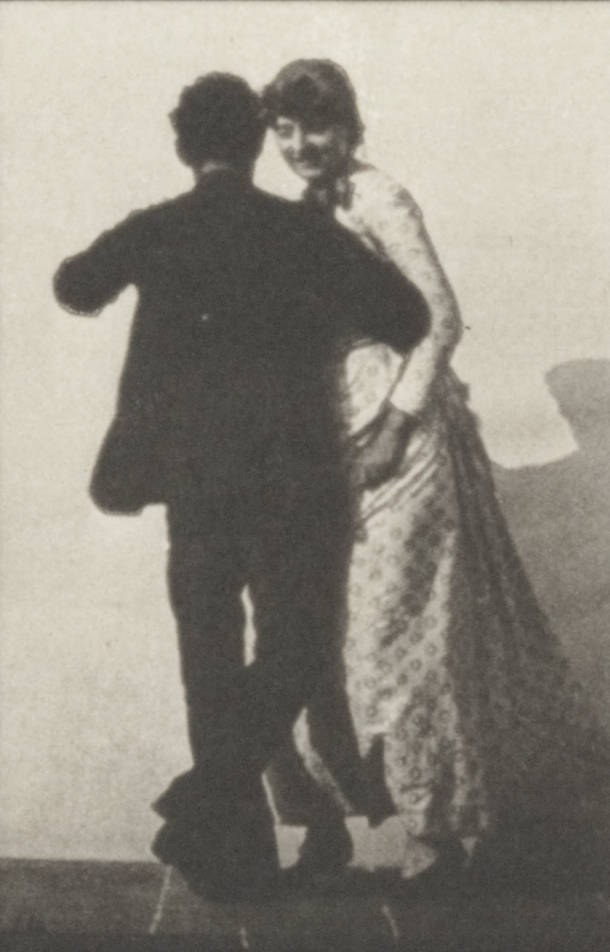 Man in dark suit and woman in light dress stand in a closed ballroom position, facing the camera in a formal waltz pose.