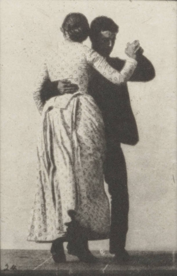 Man in dark suit and woman in patterned dress dance waltz in closed ballroom hold, woman leaning back in characteristic sway.