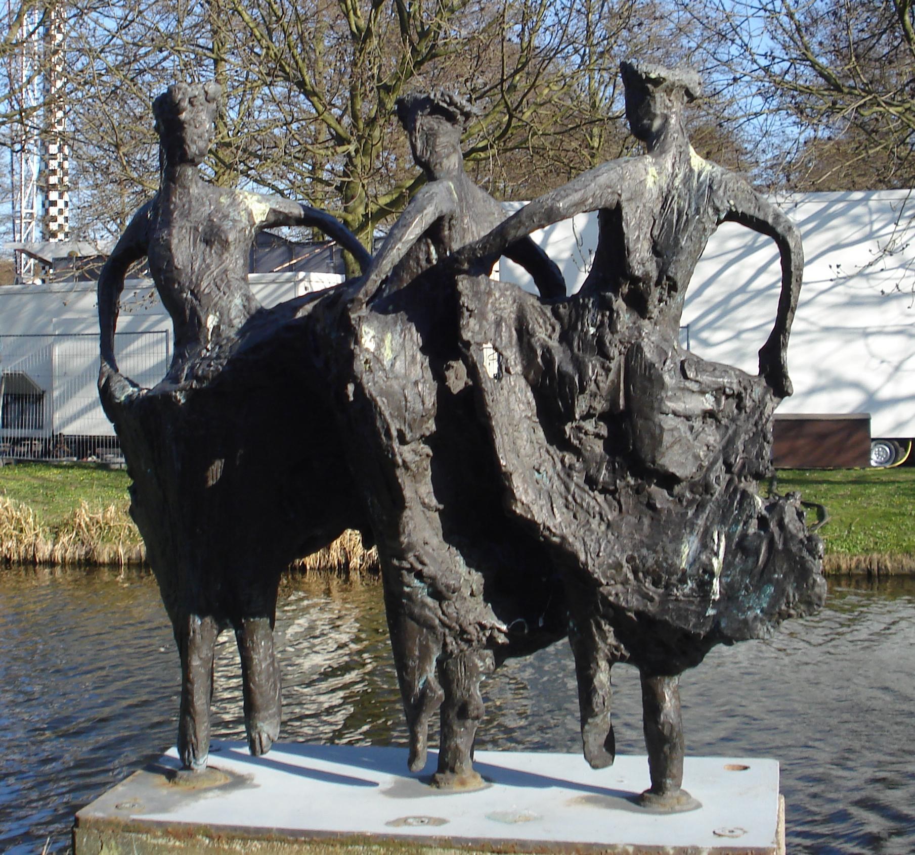 Three bronze figures in 18th-century dress stand on a waterfront platform in dynamic turning poses, representing a minuet.