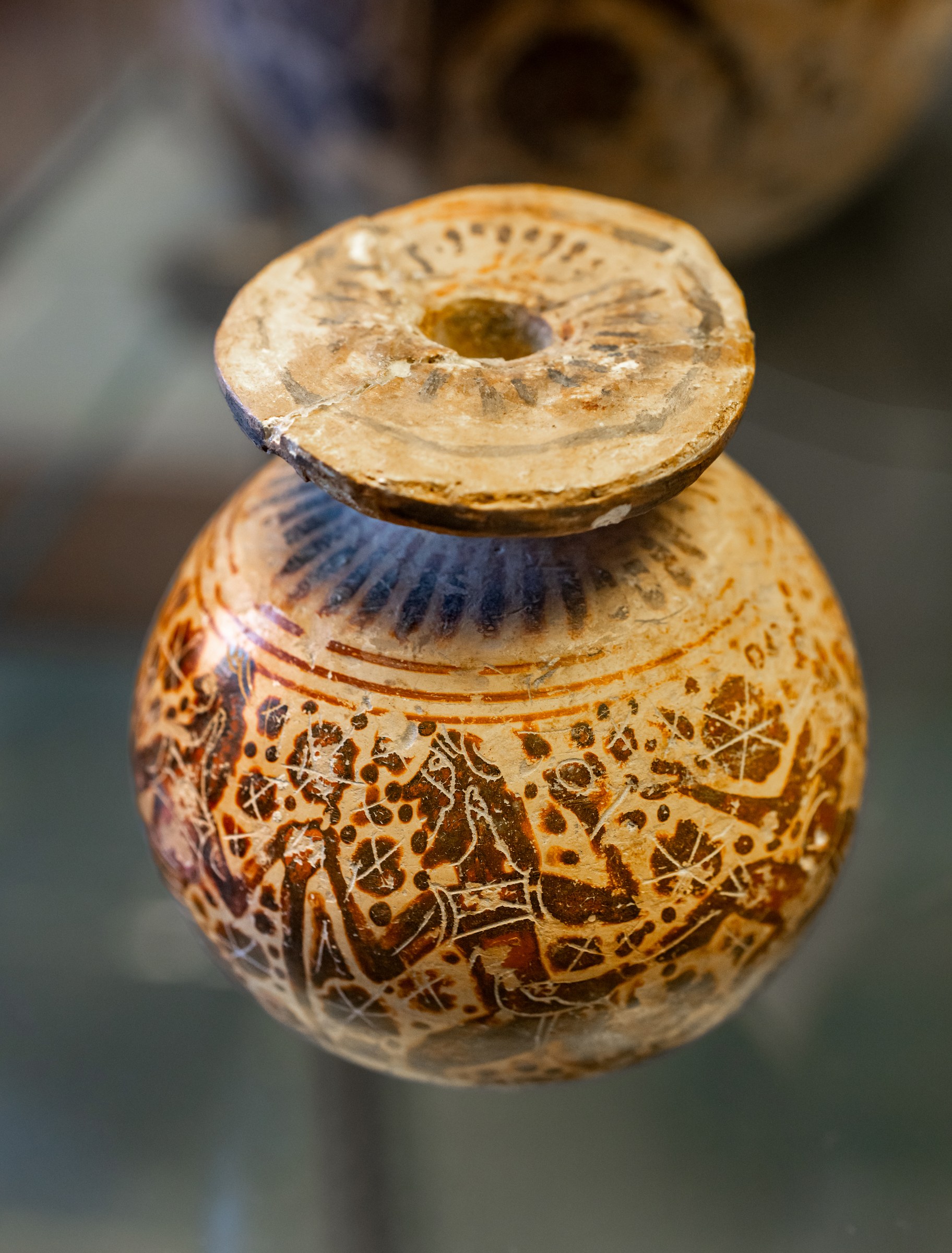Small ancient Greek pottery vessel with incised figures of padded dancers in dynamic poses around the body.